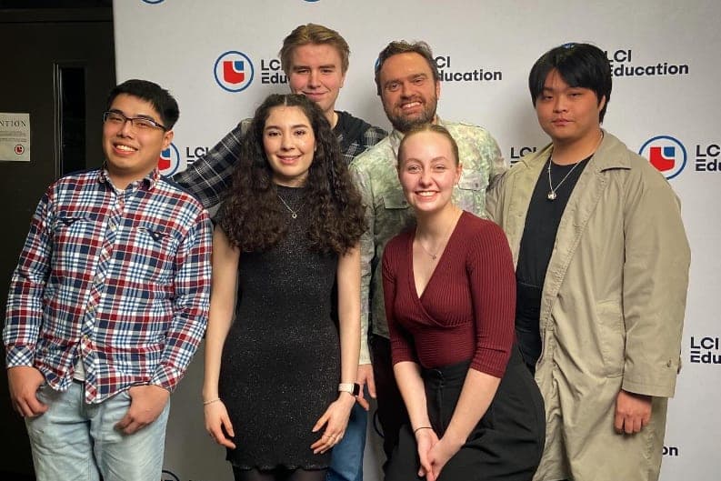 Kryshan Randel standing behind five students in front of an LCI Education banner.
